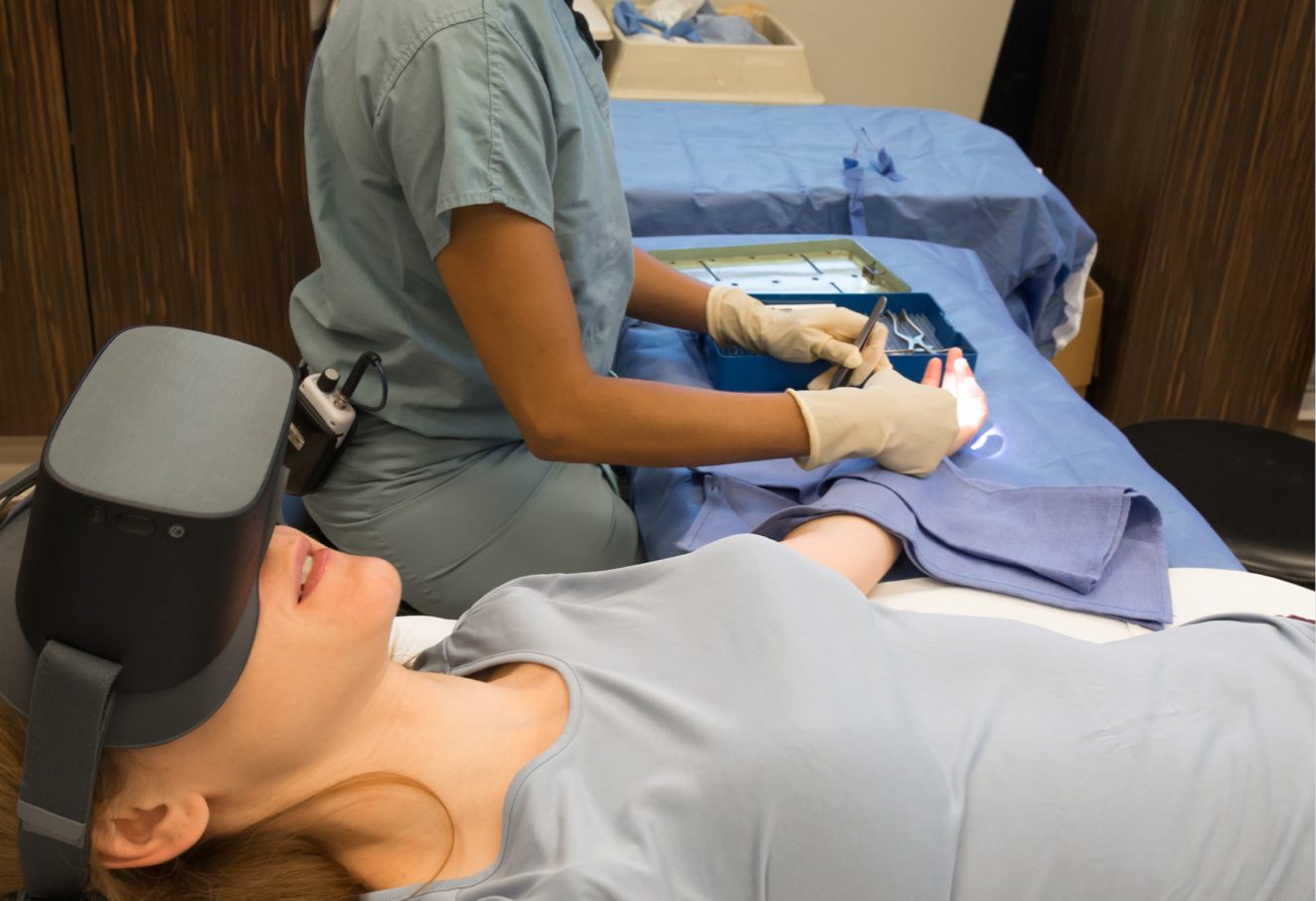A woman wears a virtual reality headset while a doctor performs a procedure.